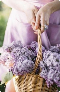 a woman holding a wicker basket with flowers in it and wearing a ring on her finger