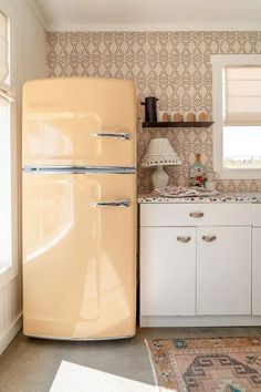 an old fashioned refrigerator in the corner of a kitchen with white cabinets and patterned wallpaper