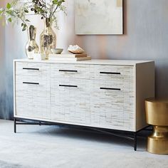 a white and gold sideboard with vases on it in front of a painting