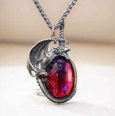 Embrace your inner strength and mythical allure with this stunning handcrafted dragon necklace. The dragon, made of 925 sterling silver, wraps protectively around a mesmerizing "Dragon's Breath" stone, which shimmers with an otherworldly mix of fiery reds and deep purples, reminiscent of mystical flames. The intricate detailing of the silver dragon captures its fierce yet elegant nature, and the sword behind the dragon adds an element of bravery and protection. The necklace hangs from a durable titanium chain, ensuring lasting quality and comfort.  This unique piece is perfect for fantasy lovers, dragon lover, or anyone looking to add a touch of magic to their jewelry collection. Material: Pendant: Sterling silver(dragon), dragon breath glass Chain: 22 inches titanium Dragon Breath, Silver Dragon Necklace, Jewelry Purple, Dragon Bracelet, Dragon Lover, Dragon Necklace, Magical Jewelry, Crystal Opal, Silver Dragon