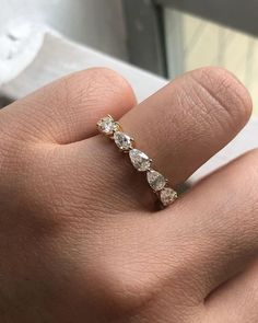 a woman's hand with a diamond ring on top of her finger, in front of a window