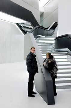 a man and woman standing next to each other in front of a stair case with an escalator