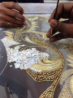 someone is working on something with gold and white designs in the background, while another hand holds a pen