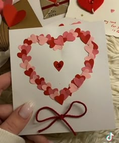 someone is holding up a heart shaped card with hearts on it and red string attached to it