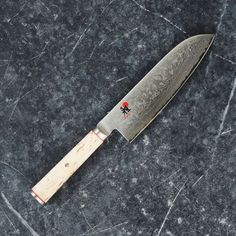 a large knife with a wooden handle sitting on top of a black countertop in front of a marble background