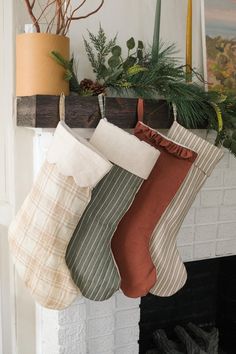 christmas stockings hanging from a mantel in front of a fireplace with greenery and pine cones