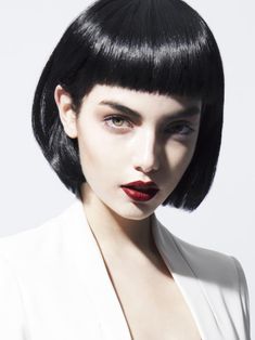 a woman with black hair wearing a white suit and red lipstick on her lips is looking at the camera