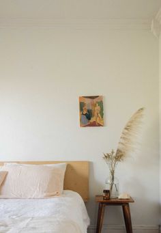 a bed with white sheets and pillows next to a painting on the wall above it