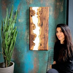 a woman sitting next to a potted plant in front of a painting on the wall