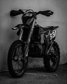 a black and white photo of a dirt bike parked in front of a wall with the number 53 on it