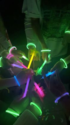 several people holding neon sticks in the dark with their hands on top of each other