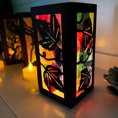 three lit candles sitting next to each other on a white table with leaves painted on them