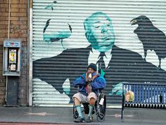 a man sitting on a bench in front of a wall with a painting of a man