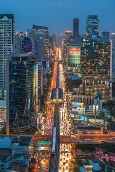 an aerial view of a city at night with lots of traffic and tall buildings in the background