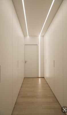 an empty hallway with white walls and wooden floors is lit by recessed lighting on the ceiling