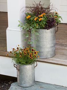 two metal buckets with flowers in them sitting on the front porch steps next to each other