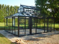 a glass house sitting on top of a cement slab in the middle of a park