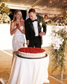 a man and woman standing in front of a cake with red roses on the top