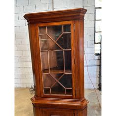 an old wooden bookcase with glass doors on the front and bottom shelves, sitting against a white brick wall