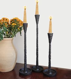 three black candles are sitting next to a vase with yellow flowers