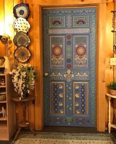 a blue door with intricate designs on it in front of a book shelf and vases