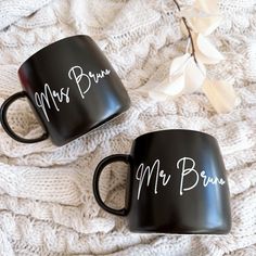 two black coffee mugs sitting on top of a white blanket