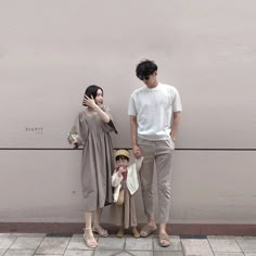 a man and woman standing next to each other near a wall with a child on it