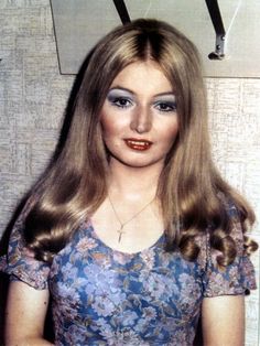 an old photo of a woman with long blonde hair and blue eyeshadow, wearing a floral dress