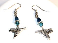 Hummingbirds symbolize hope and levity. These earrings capture the magic and mystery that is the hummingbird! One bird is facing left and one bird is facing right. Earrings measure approximately 47mm (about 1-¾ inches) from the top of the surgical stainless steel ear wire to the bottom of the silver tone charms which are about 17mm wide with two colors of blue crystal accents.  Arrives gift boxed with a jewelry pouch! Hummingbird Earrings Silver Blue Crystal Jewelry, Bird Jewelry Gift Handmade, Hummingbird Earrings, Surgical Steel Earrings, Bird Watcher, Diy Wire Jewelry, Professional Jewelry, Bird Jewelry, Original Jewelry, Earrings Blue, Gift Handmade