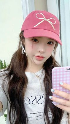 a girl with long hair wearing a pink hat and holding a cell phone in her hand