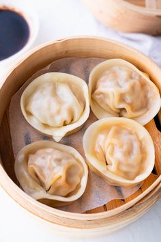 four dumplings in a wooden bowl with sauce on the side