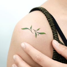 a woman's arm with a small green leaf tattoo on the left side of her shoulder