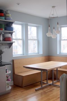 a kitchen with a table and benches in the corner, next to two windows that look out onto the street