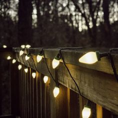 some lights are hanging on the side of a wooden fence in front of dark trees