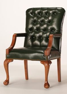 a green leather chair with wooden legs and arm rests against a white wall in front of it