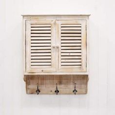 a wooden shelf with two doors and hooks on the wall next to a white wall