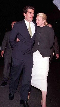 a man in a suit and tie walking next to a woman wearing a white skirt