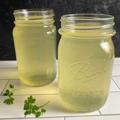 two jars filled with green liquid sitting on top of a white tile floor next to each other