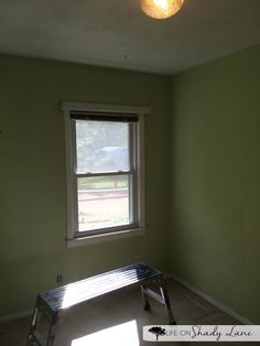 an empty room with green walls and a small bench in the corner next to a window