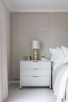 a white bed sitting next to a nightstand with a lamp on top of it in a bedroom