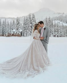 a bride and groom are kissing in the snow with trees in the backgroud