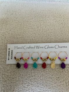 five wine glass charms are displayed on a white card with the name hand crafted wine glass charms