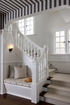 a white staircase with black and white striped curtains on the windowsill, and a bench in front of it