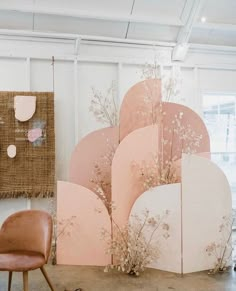 an arrangement of pink and white shapes on display in a room with a chair, rug and wall hangings