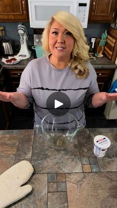 a woman standing in front of a kitchen counter holding out her hands and making something