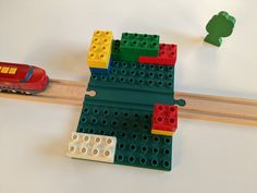 a toy train is on the tracks with legos next to it and a red car