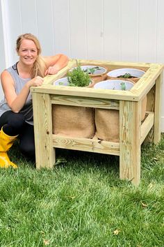 a woman kneeling in the grass next to a wooden planter box with plants inside