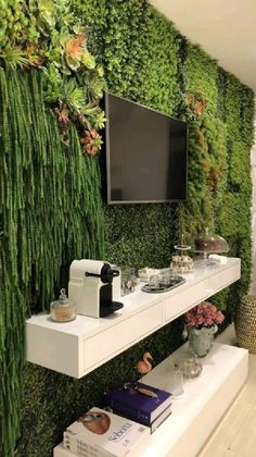 a tv mounted to the side of a wall covered in green plants and succulents