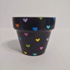 a black pot with multicolored hearts painted on the outside and inside, sitting on a white surface