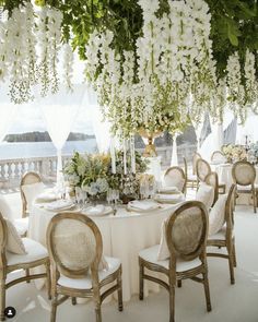 a table set up with white flowers and greenery hanging from the ceiling over it